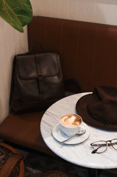 A cappuccino on a marble cafe table with a hat and glasses, creating a cozy vibe.