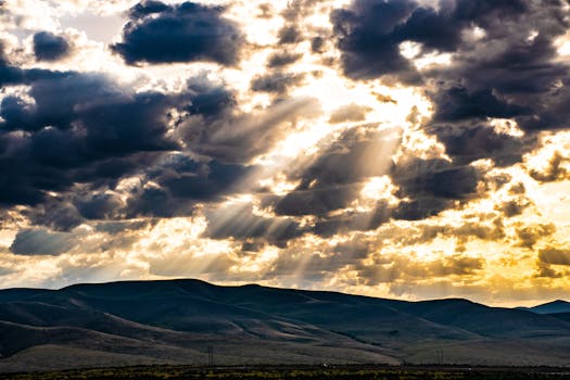 Captivating sunset with sunrays piercing through clouds over scenic hills.