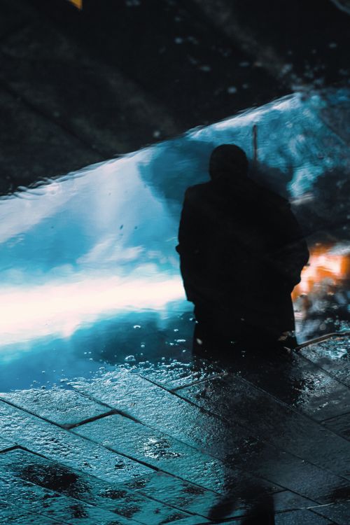 Free Moody silhouette reflection in a puddle on a dark urban sidewalk. Stock Photo