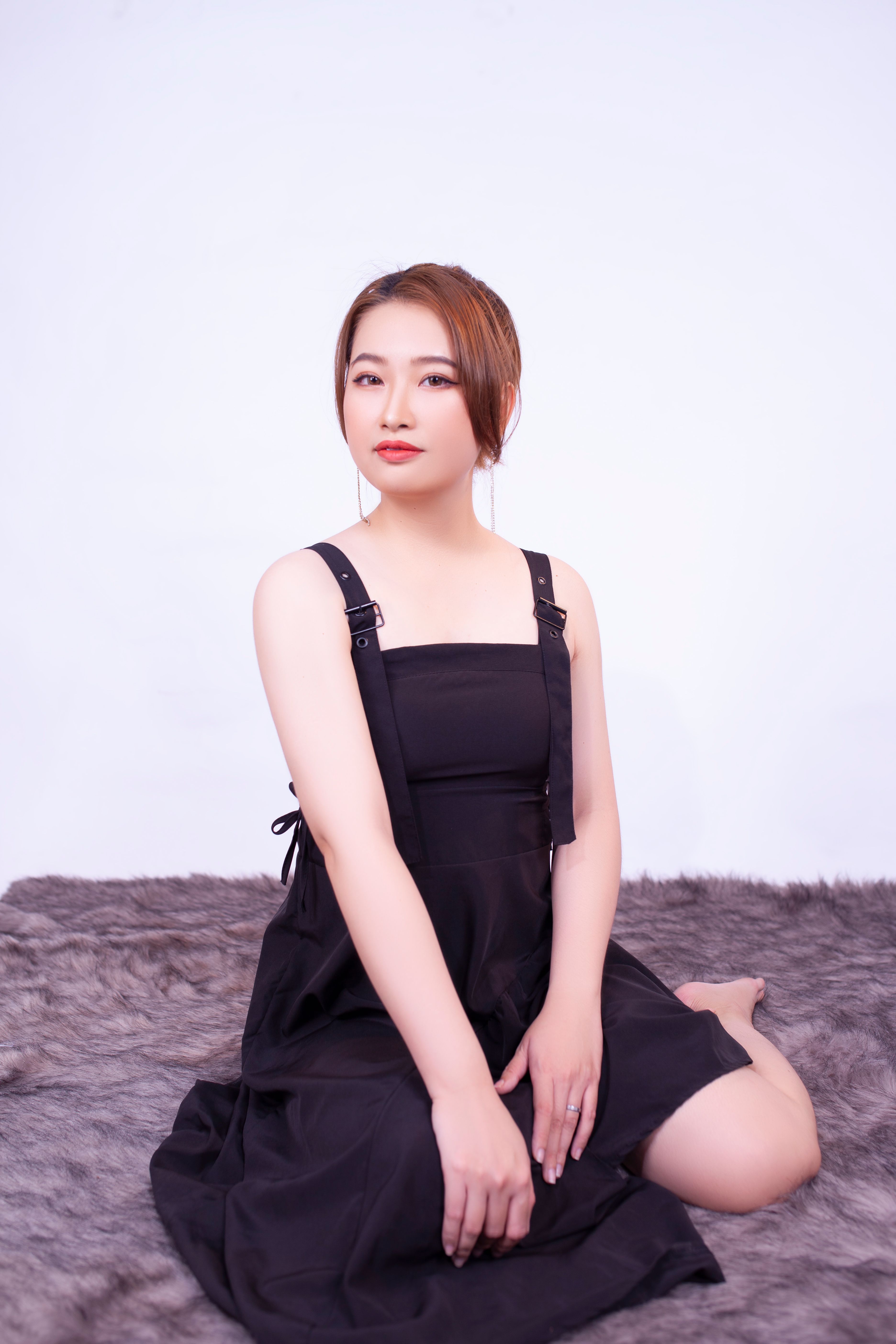 Studio portrait of an Asian woman in a black dress sitting gracefully on a fur rug.