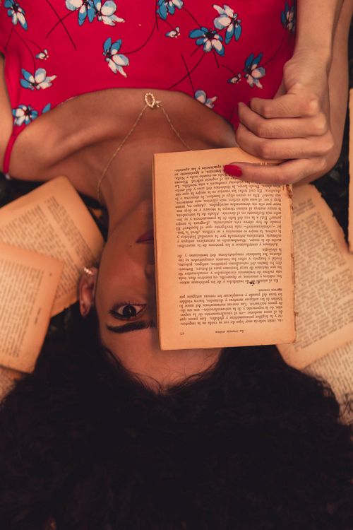 Free Brunette woman in floral dress reading a book while lying on the floor indoors. Stock Photo
