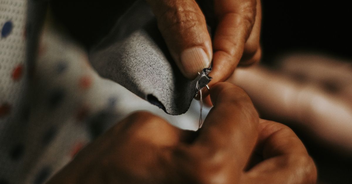 close-up of hands sewing a patch onto a pair of denim jeans