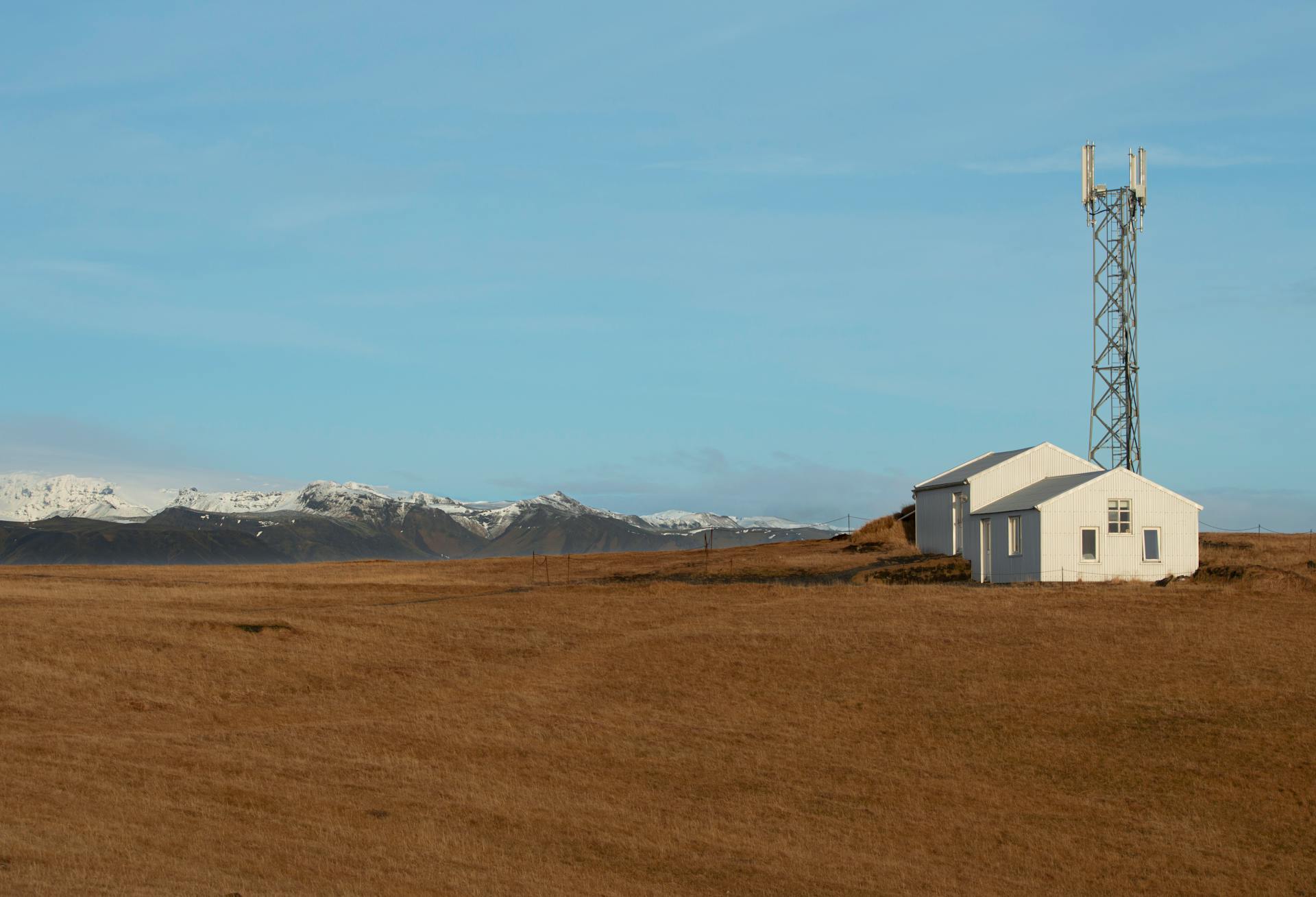 Idyllic Iceland scene featuring a farmhouse and communication tower against mountains.