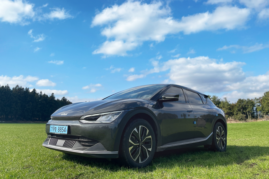 A sleek black car parked on a grassy field under a bright blue sky with clouds.