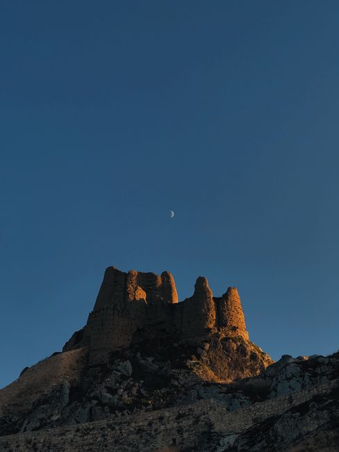 Captivating crescent moon over ancient rock formation in Turkey's evening landscape.