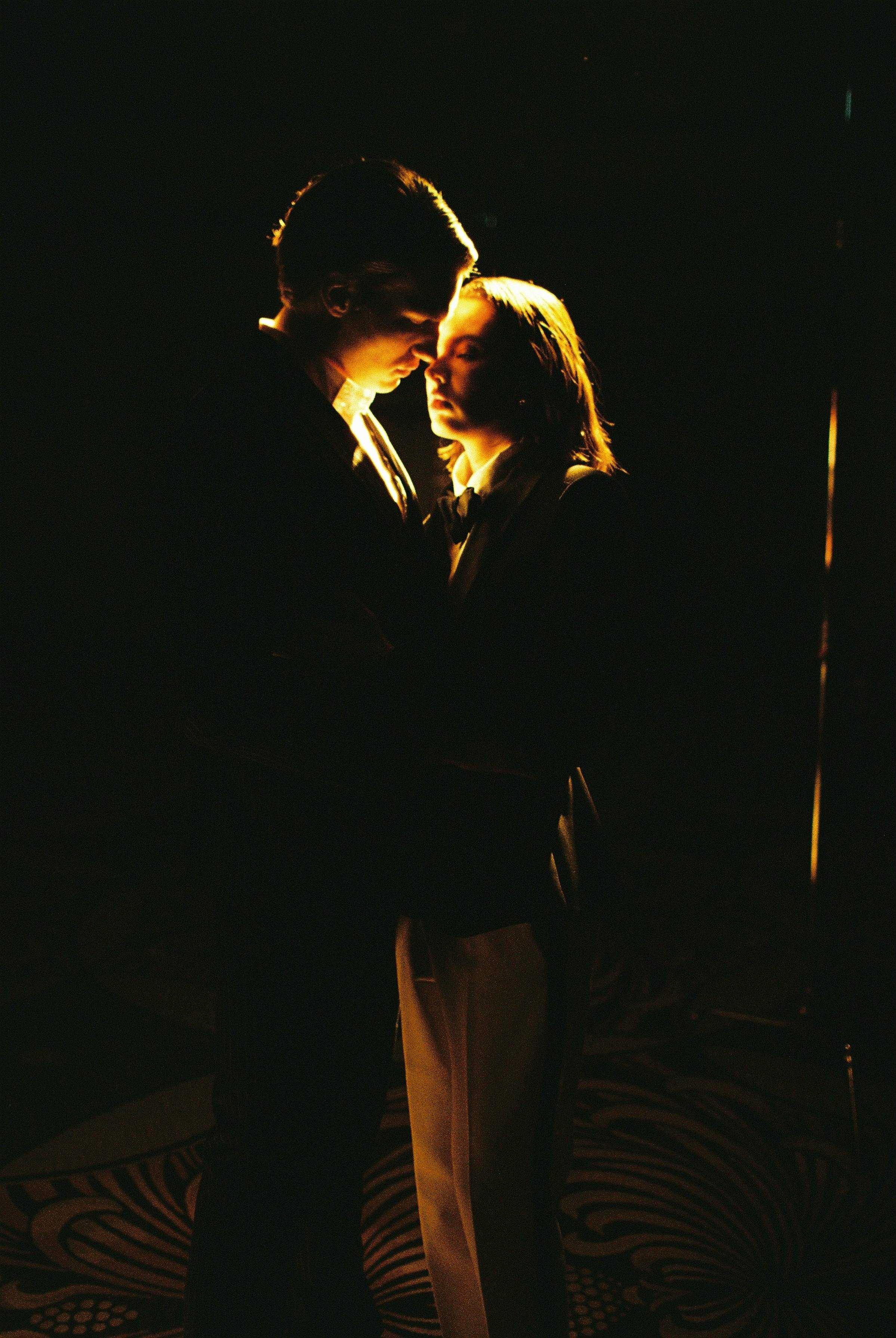 A couple in an intimate embrace, illuminated against a dark background, exuding romance.