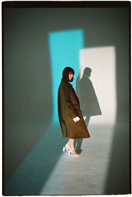 Fashionable woman in coat and heels casting striking shadows indoors.