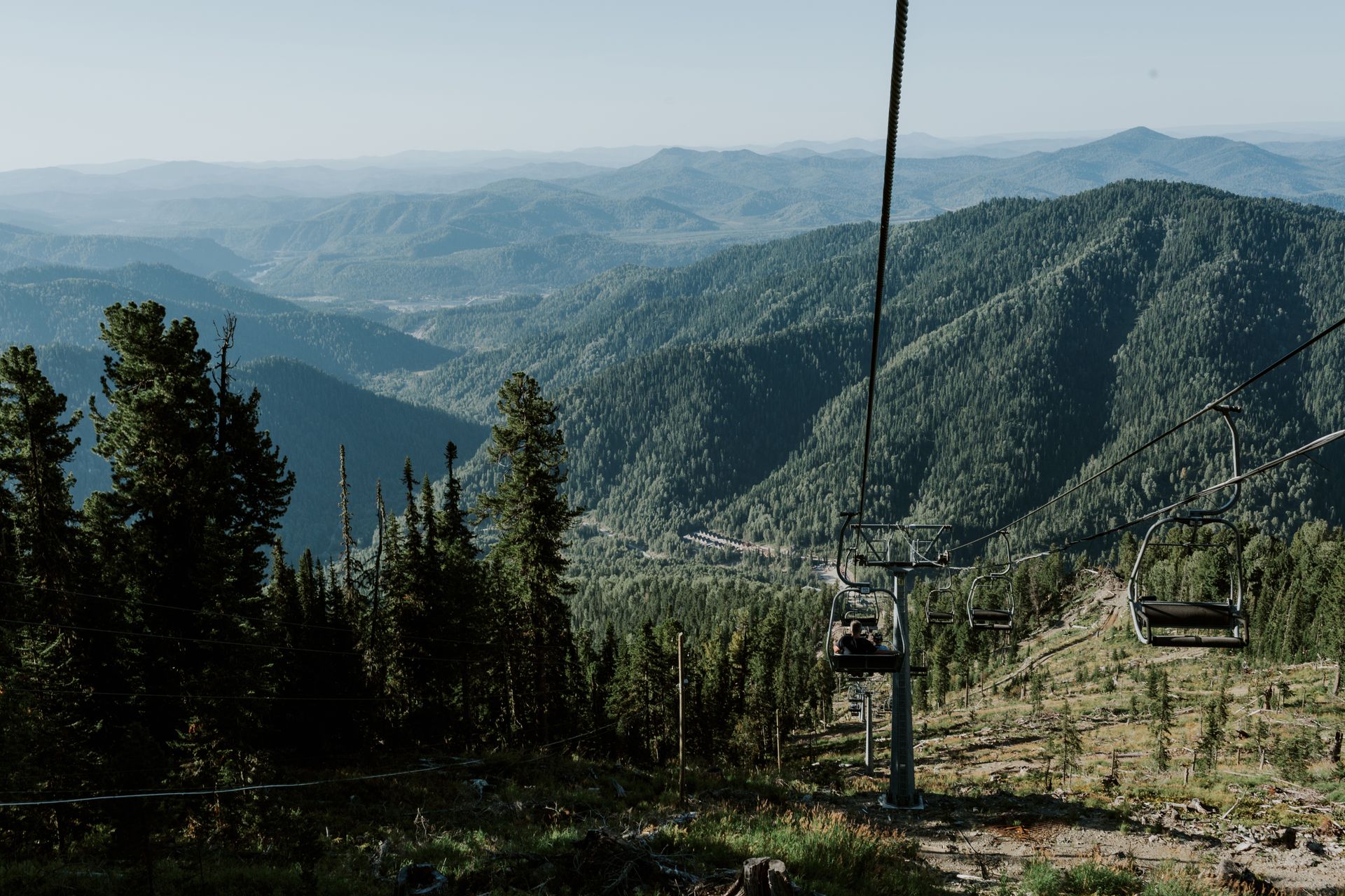 Scenic view of a mountain range with lush evergreens and a ski lift under a clear sky.