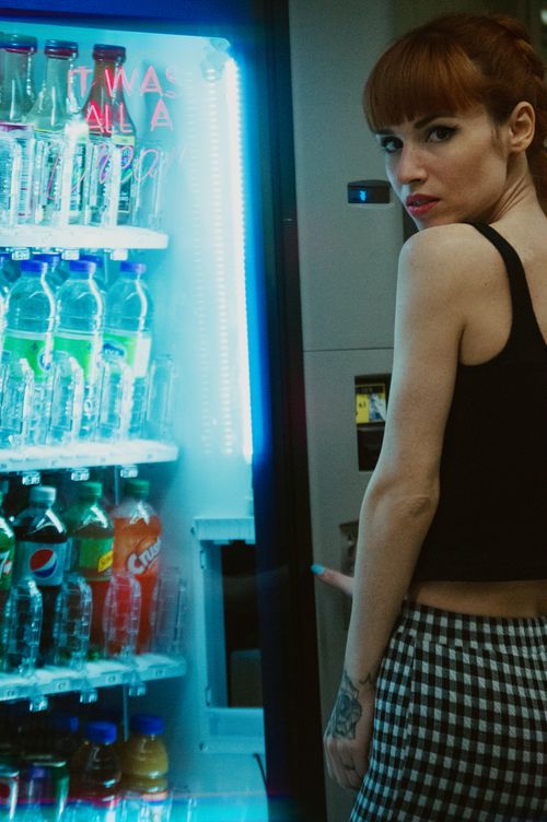 Free A woman looks over her shoulder while selecting a drink from a vending machine. Urban setting with neon lights. Stock Photo