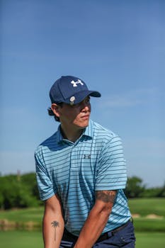 Man with tattoos and cap preparing to swing on a sunny golf course.