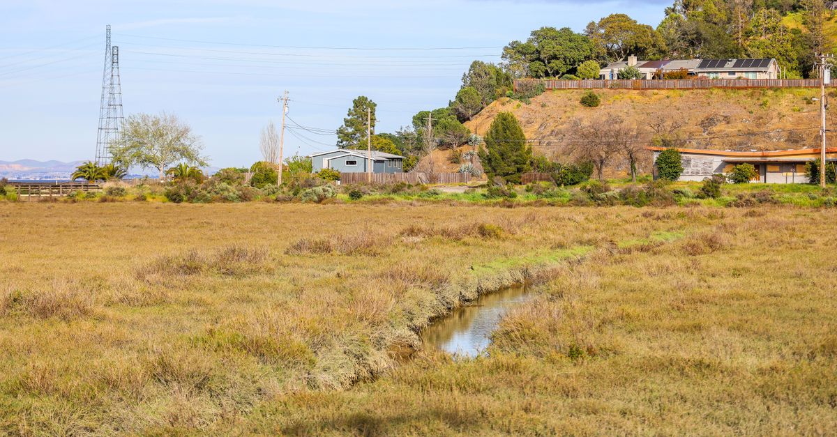 Serene countryside view with brown grass field and small water canal, set below a hilltop.