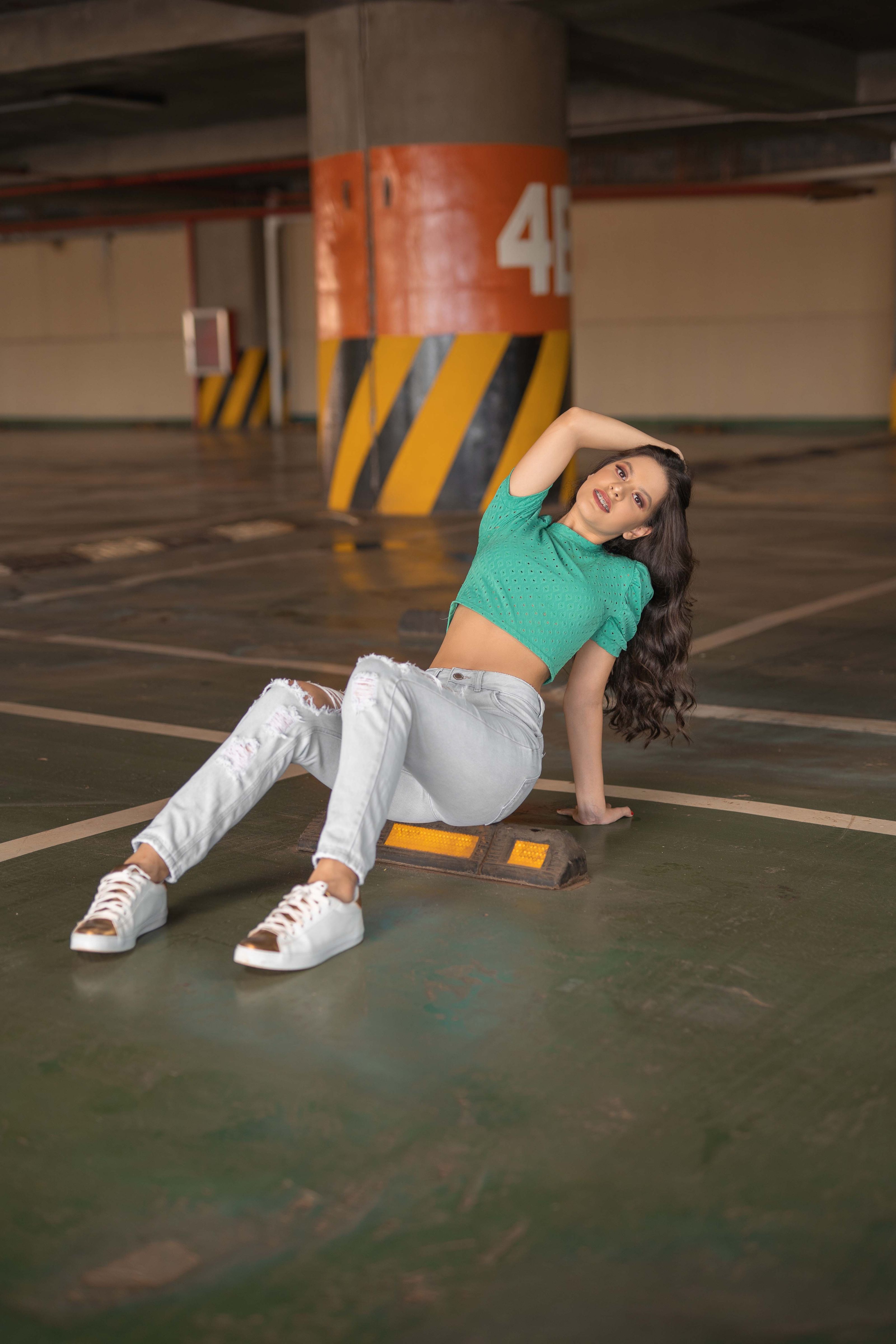Mulher estilosa sentada na calçada em um estacionamento coberto, adotando uma pose casual.