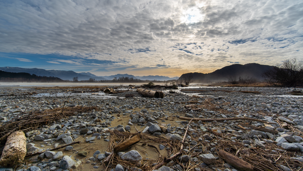 Scenic view of a rocky riverbed with mountains and cloudy skies in the background at twilight.