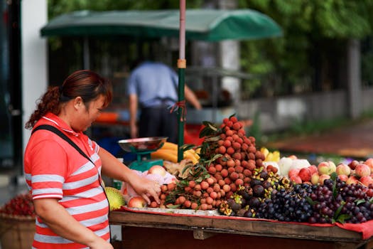 A female vendor arranging fruits at her street stall, featuring lychees, grapes, and more.
