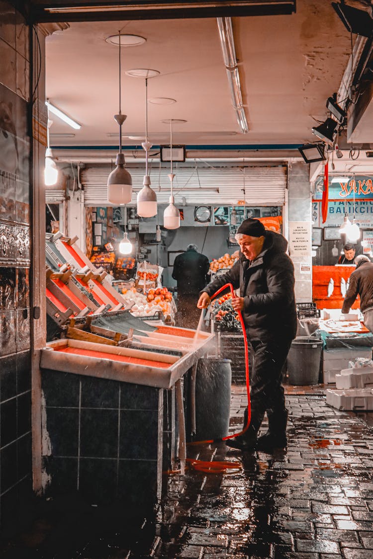 An Elderly Man Cleaning His Stall Using A Water Hose