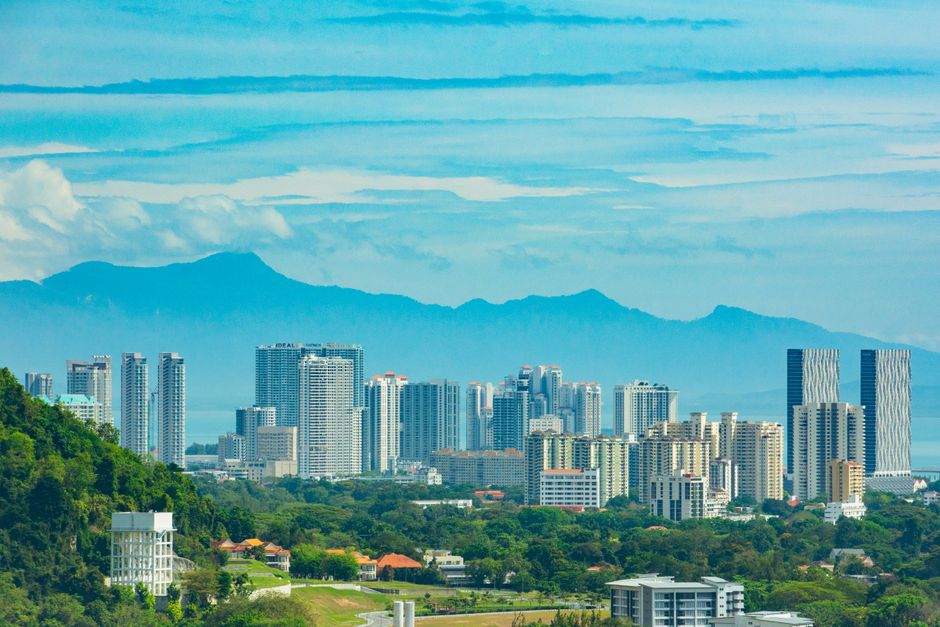 View of the Tanjung Tokong skyline with skyscrapers and lush greenery against mountains.