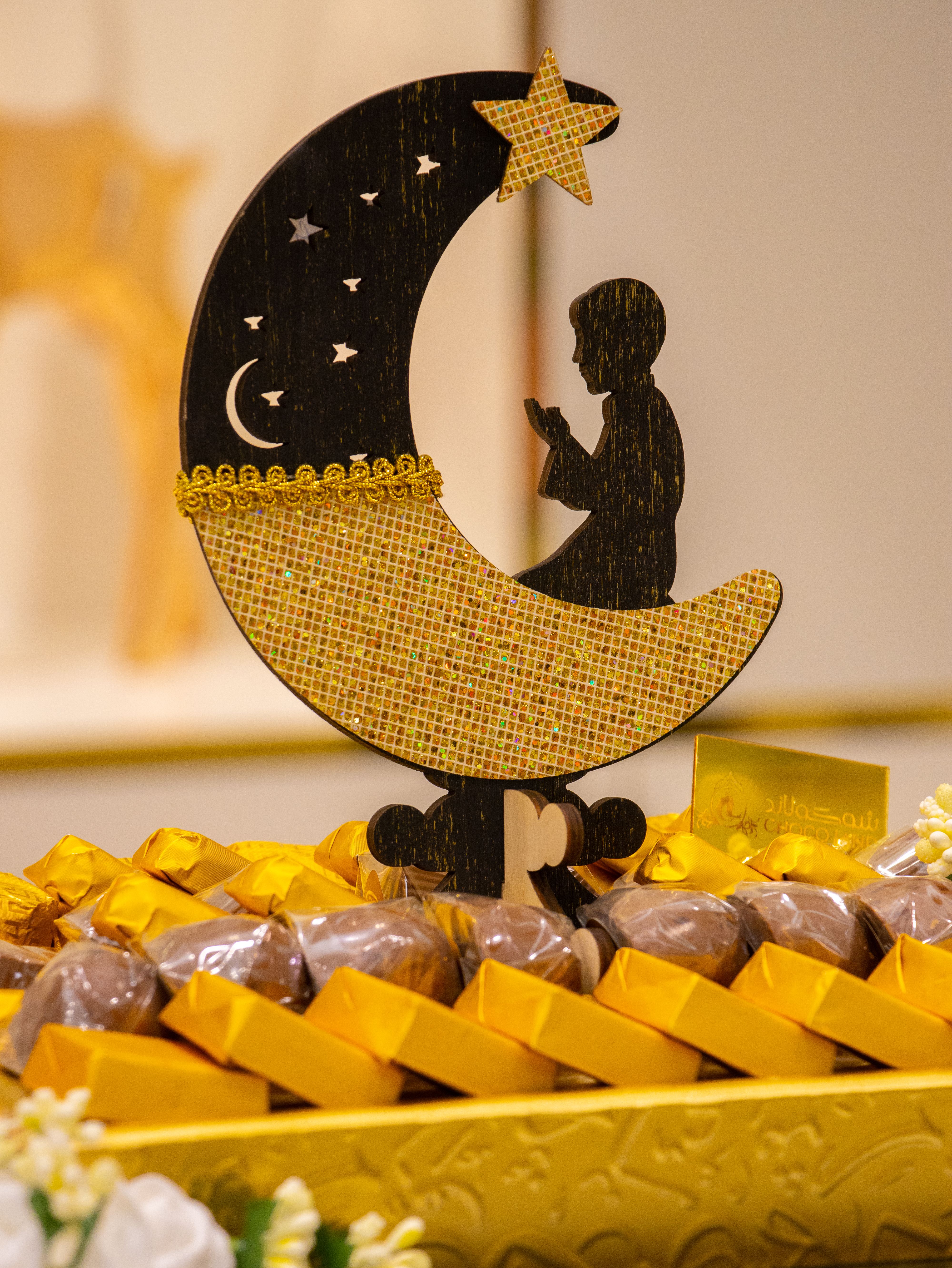 A festive Ramadan decoration featuring a crescent moon ornament among wrapped chocolates.