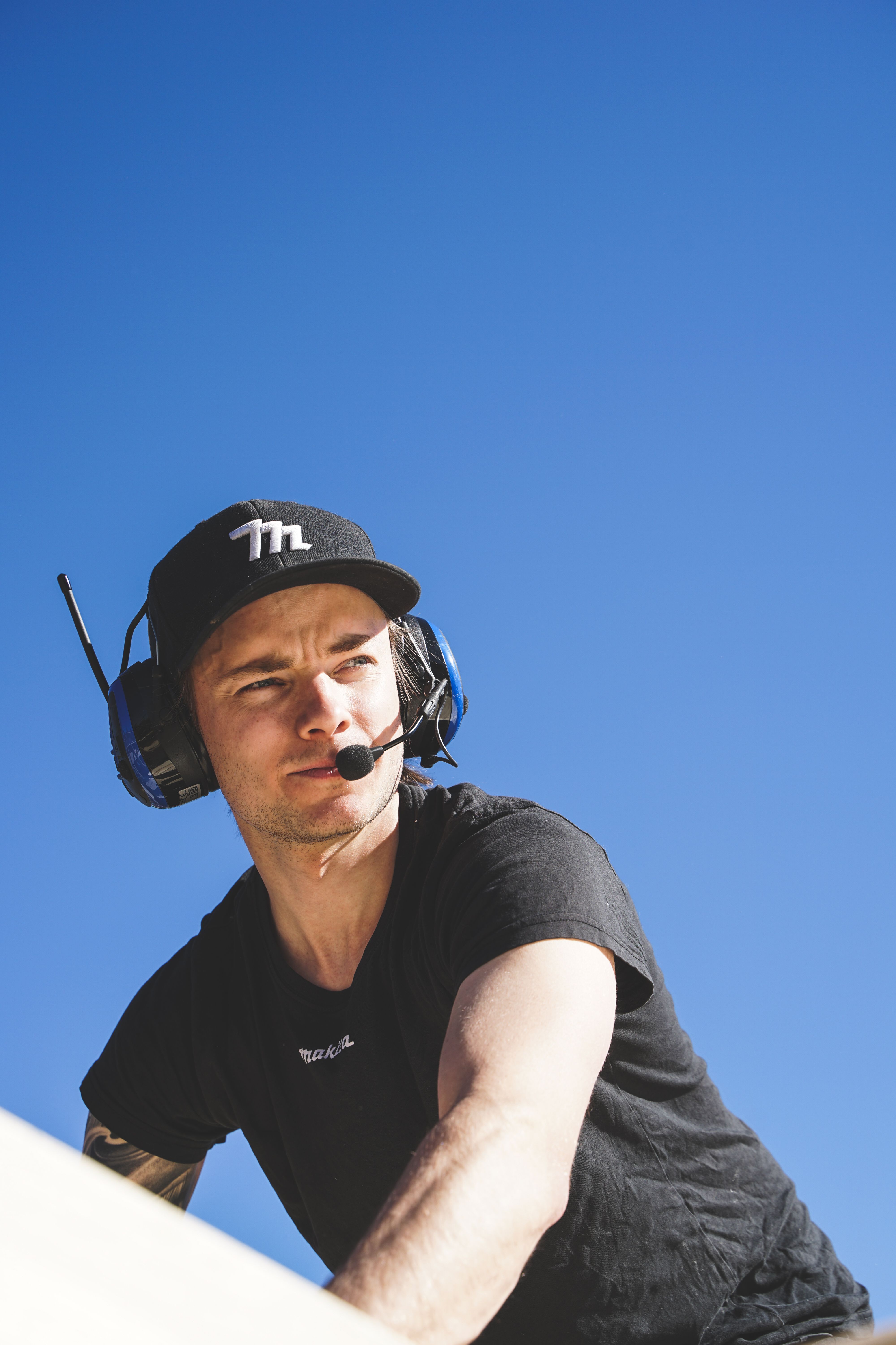 Young man in headset looks up, against a clear blue sky, in a low-angle shot.
