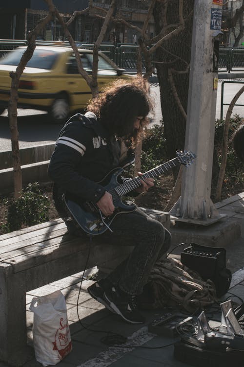 A Man in Black Jacket Playing Electric Guitar on the Street