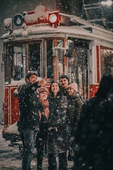 Friends smile and take a selfie in the snow by a vintage tram during a winter snowfall.