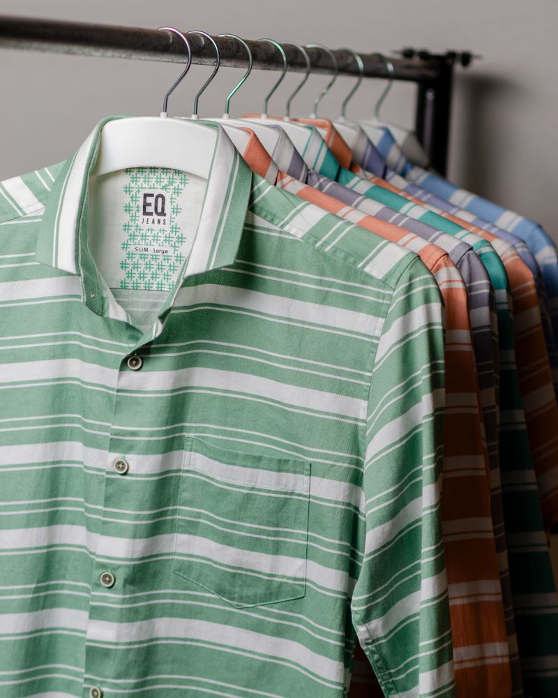 Deretan kemeja katun motif garis warna-warni tergantung di hanger