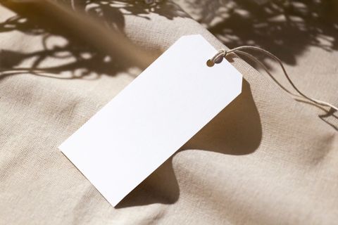 Blank cream fabric tag tied to soft beige cloth in window shadow