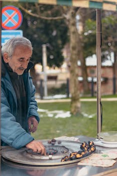 Elderly man roasting chestnuts on a street vendor stall in winter outdoors.