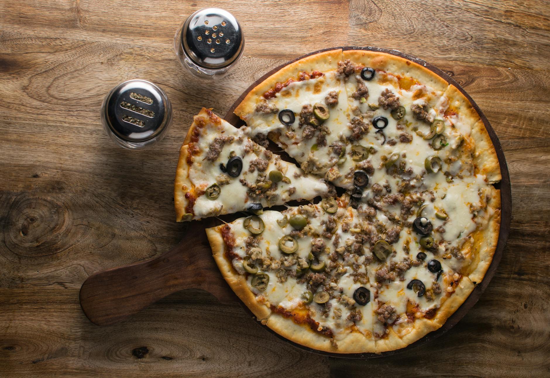 Aerial view of a freshly baked pizza with olives and sausage on a wooden paddle, showcasing food photography.