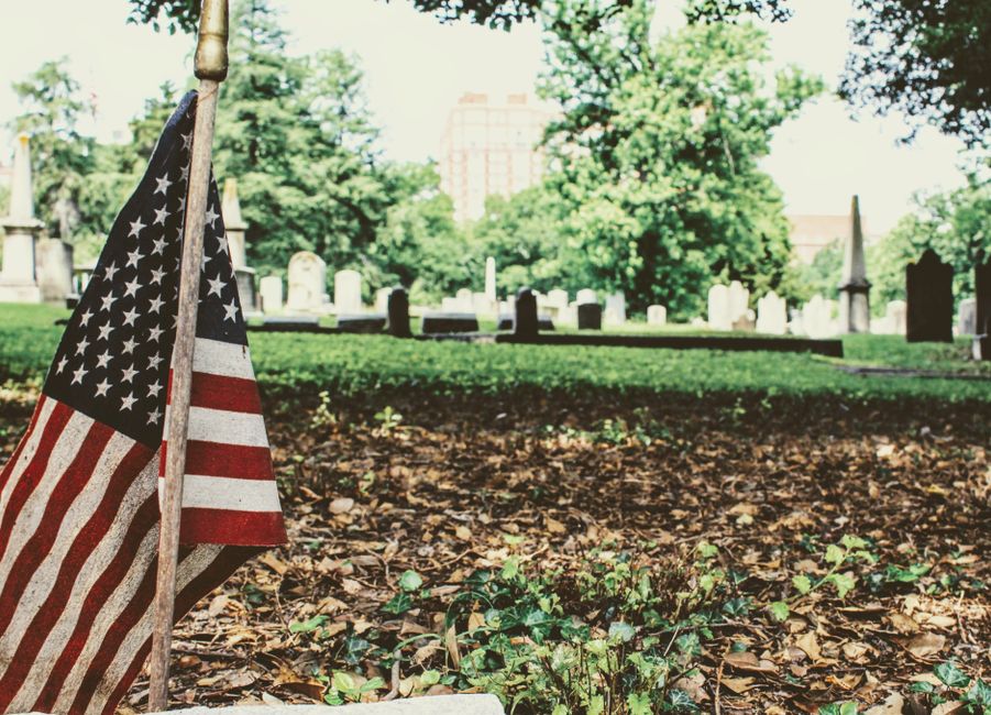 American flag and military headstone at a national cemetery American flag and military headstone at a national cemetery