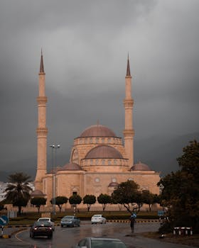 Stunning mosque in Oman with towering minarets under a dramatic cloudy sky, attracting visitors and locals.