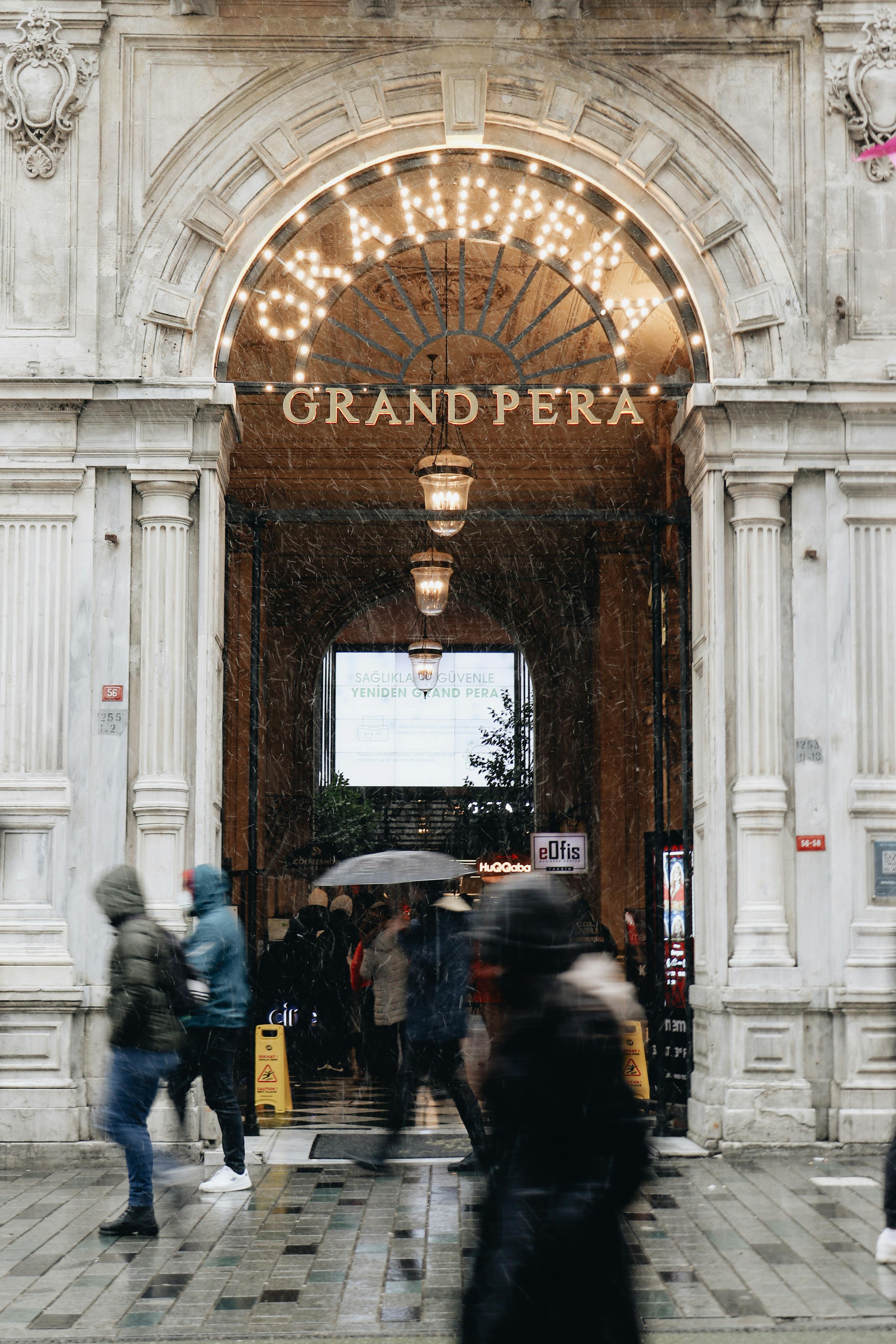 Busy entrance at Grand Pera, Istanbul, featuring people in motion on a rainy day.