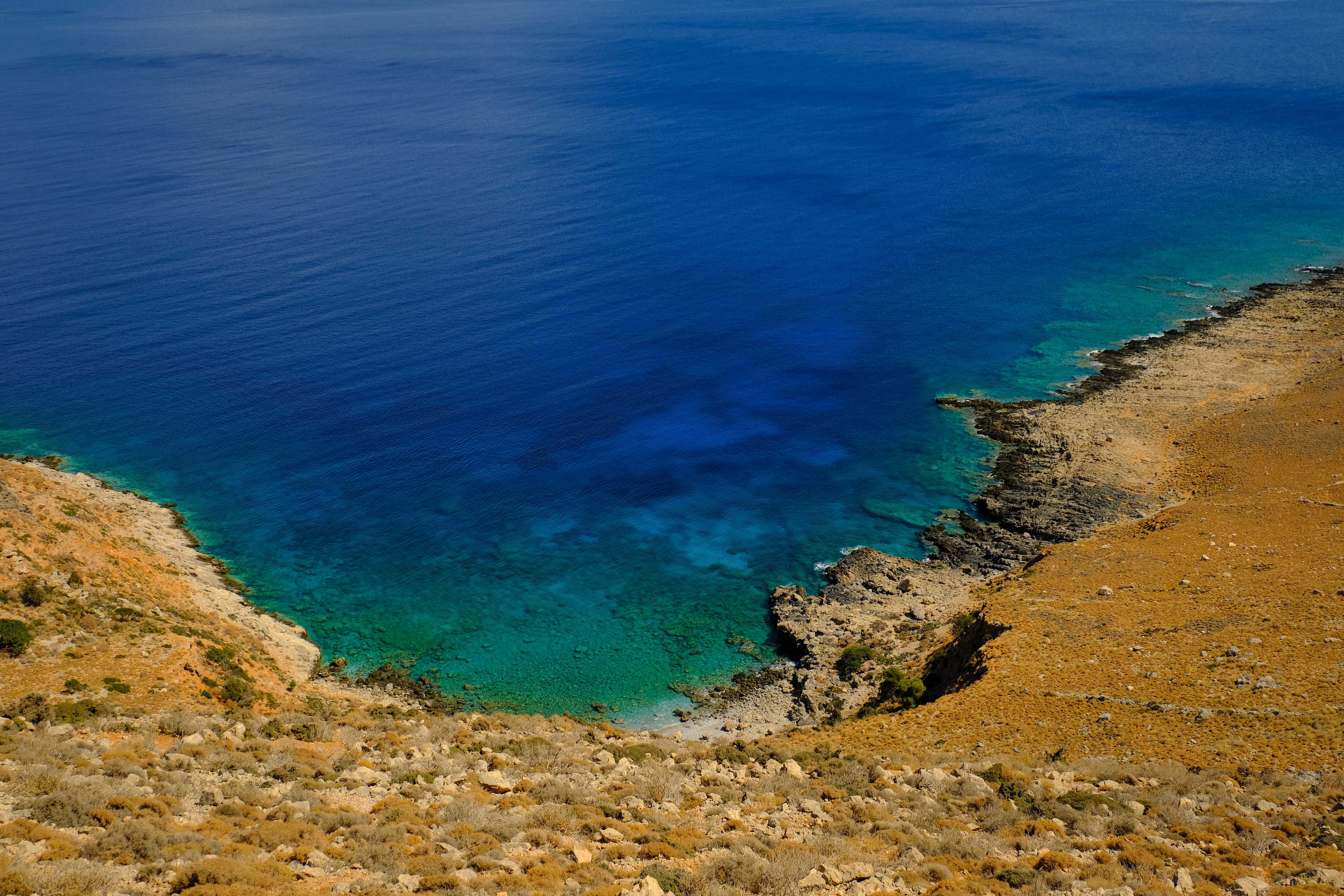 Stunning aerial view of a rocky coastline with clear blue water and arid terrain. - Photo by Francesco Ungaro on Pexels