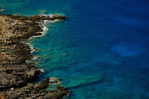 Free A vivid aerial shot showcasing the stunning contrasts between rocky shore and deep blue ocean waters. Stock Photo