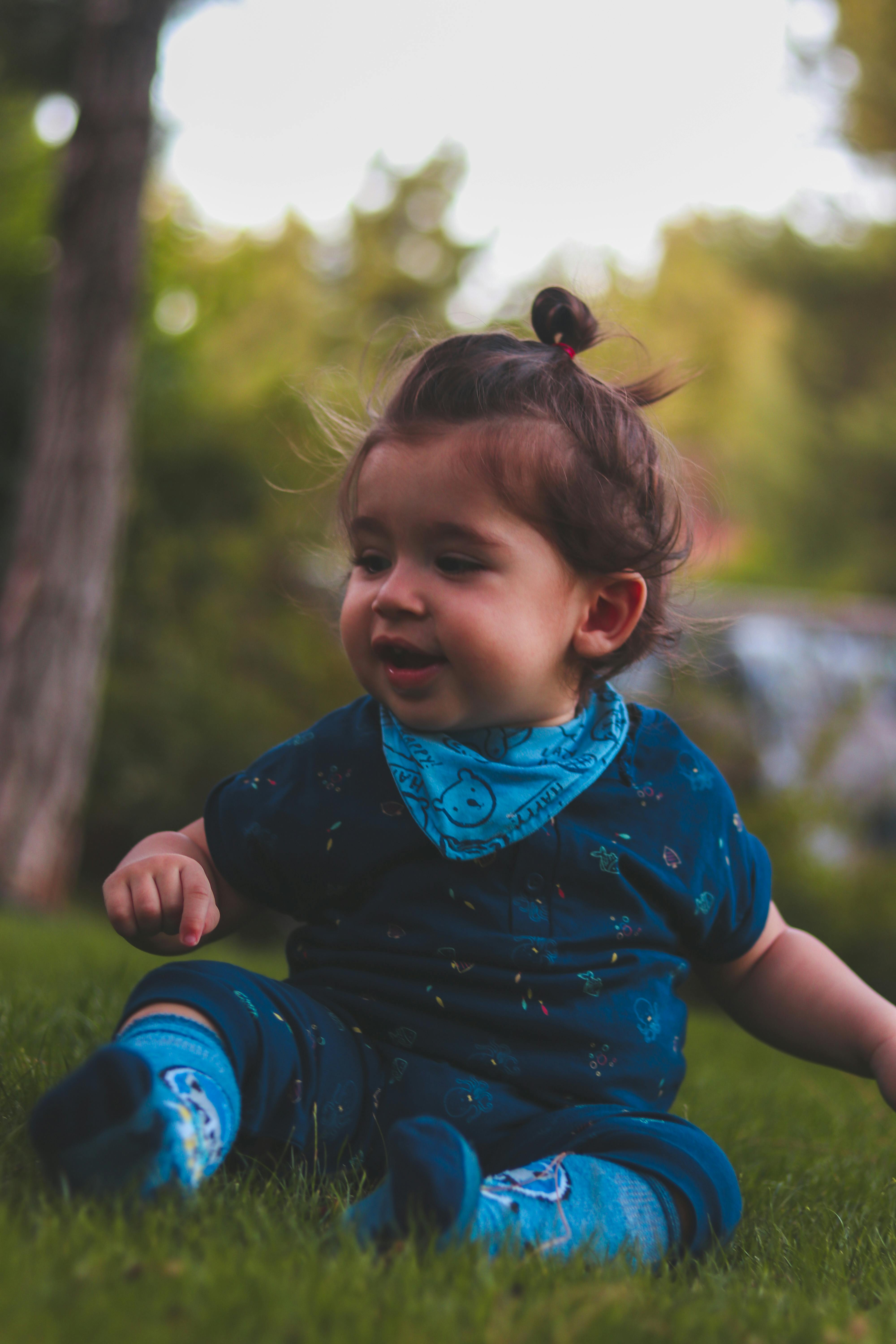 photo of baby wearing blue onesie and socks sitting on green grass