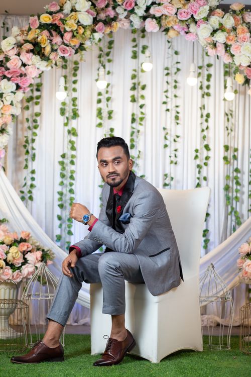 Free Stylish Indian groom in a grey suit posing indoors at a vibrant floral wedding backdrop. Stock Photo
