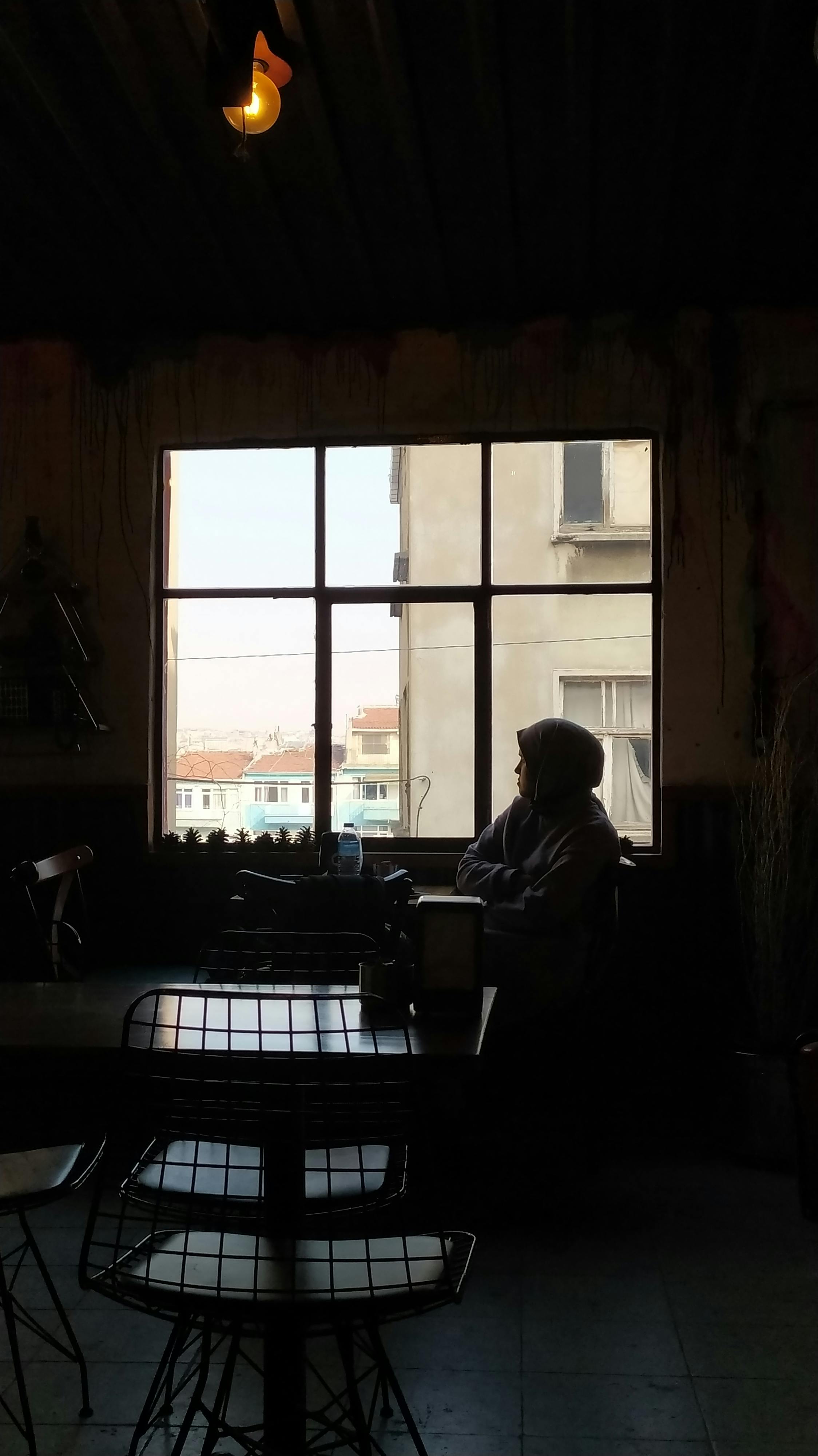 A person in a hoodie sitting by a window in a dimly lit room in Istanbul.