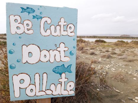 A hand-painted sign on Limassol beach promoting environmental conservation with the message 'Be Cute Don't Pollute.'