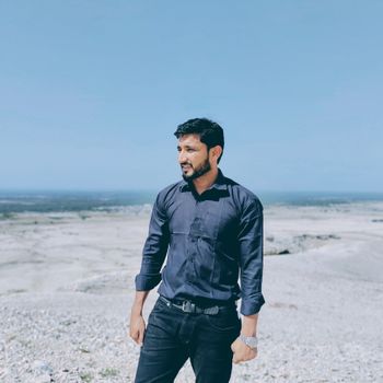 Man in dark shirt on a bright, sandy beach in Sindh, Pakistan, under a clear sky.