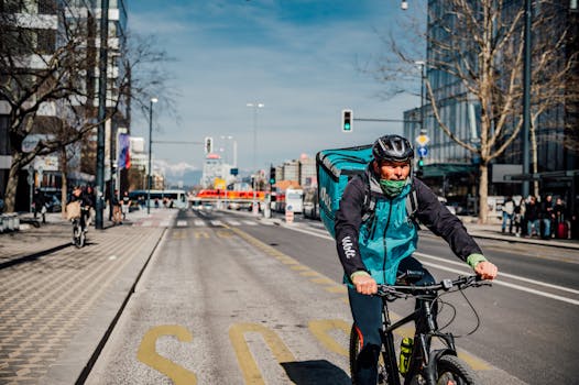 A delivery cyclist rides on a busy street in Ljubljana on a sunny day, showcasing urban logistics.
