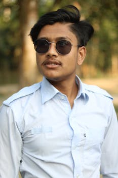 Young man in sunglasses poses confidently outdoors in a bright white shirt.