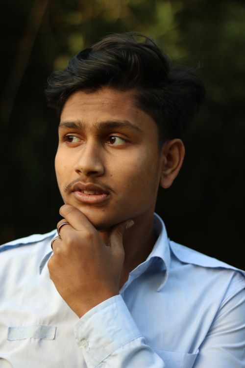 Free Portrait of a young man in a white shirt posing thoughtfully outdoors in natural light. Stock Photo