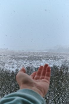 A hand reaching out towards a snow-covered field during winter, illustrating a serene winter landscape.