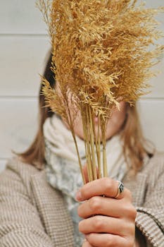 Close-up of a woman holding a bunch of dried grass, creating a natural texture.