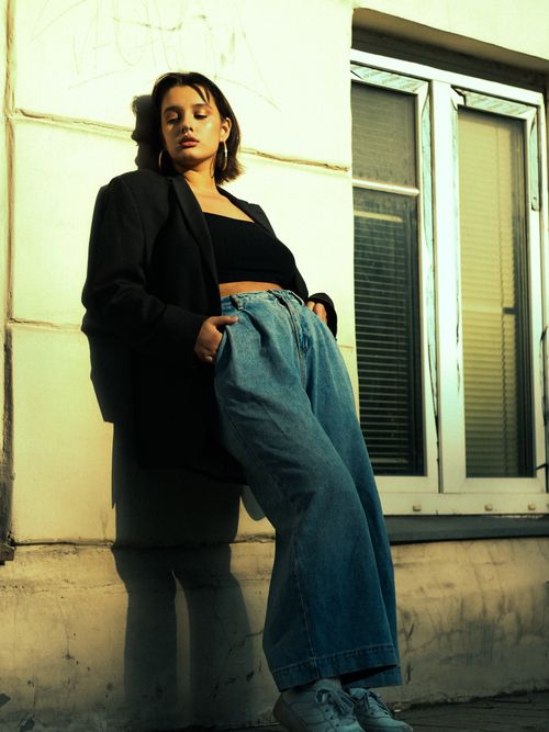 Free Stylish young woman posing against a city building wall in casual attire. Stock Photo