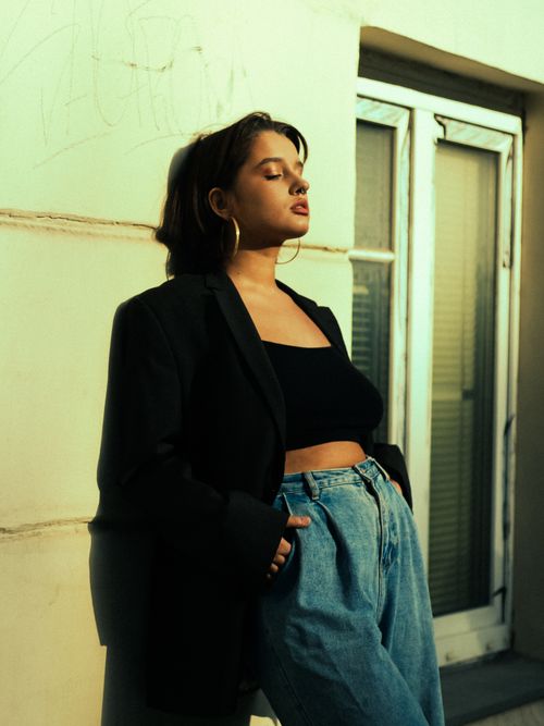 Free Young woman in a casual urban setting, wearing stylish attire and leaning against a wall. Stock Photo