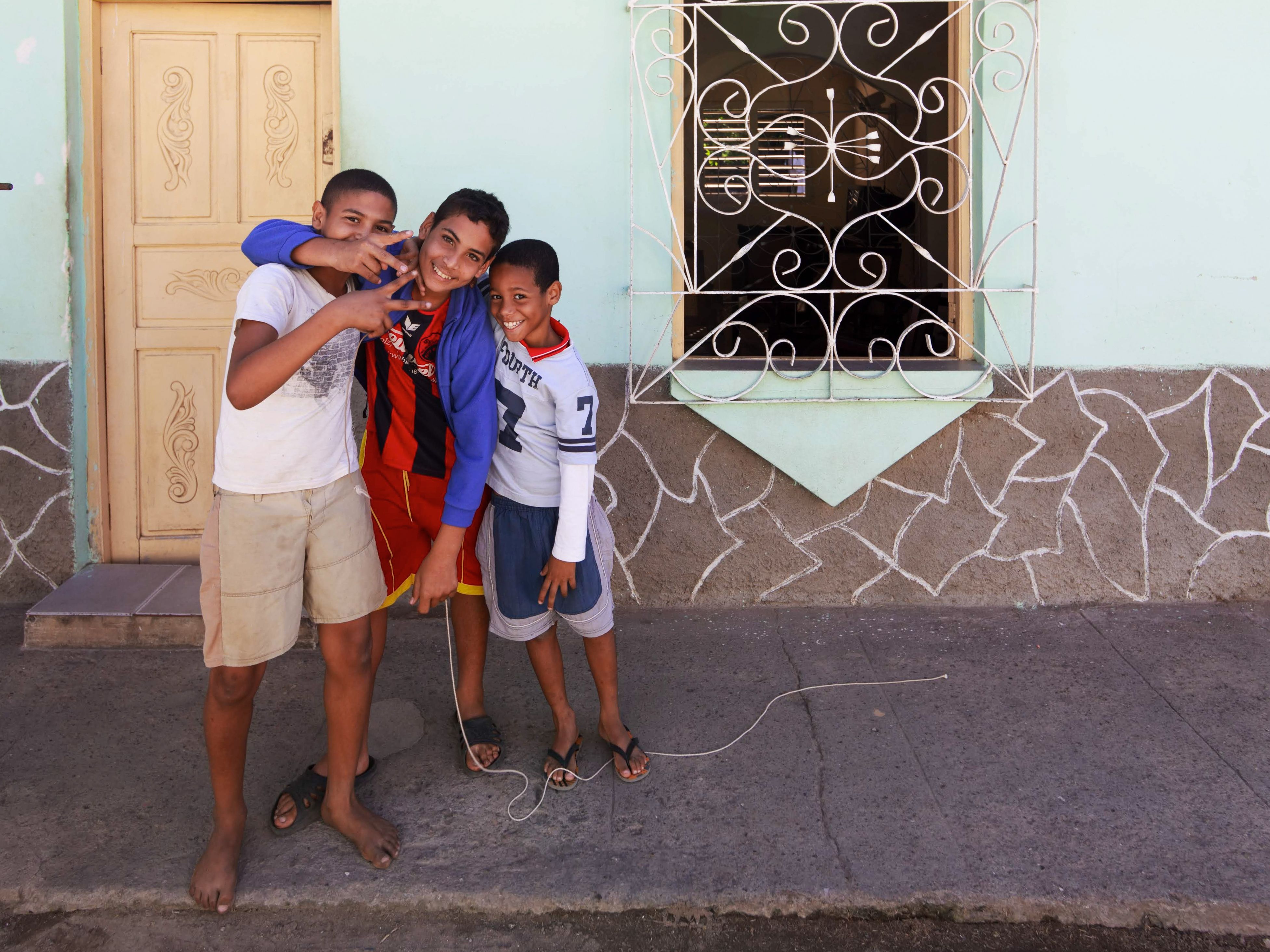 Three young boys having fun and posing outside a house on a sunny day, showcasing friendship and joy.