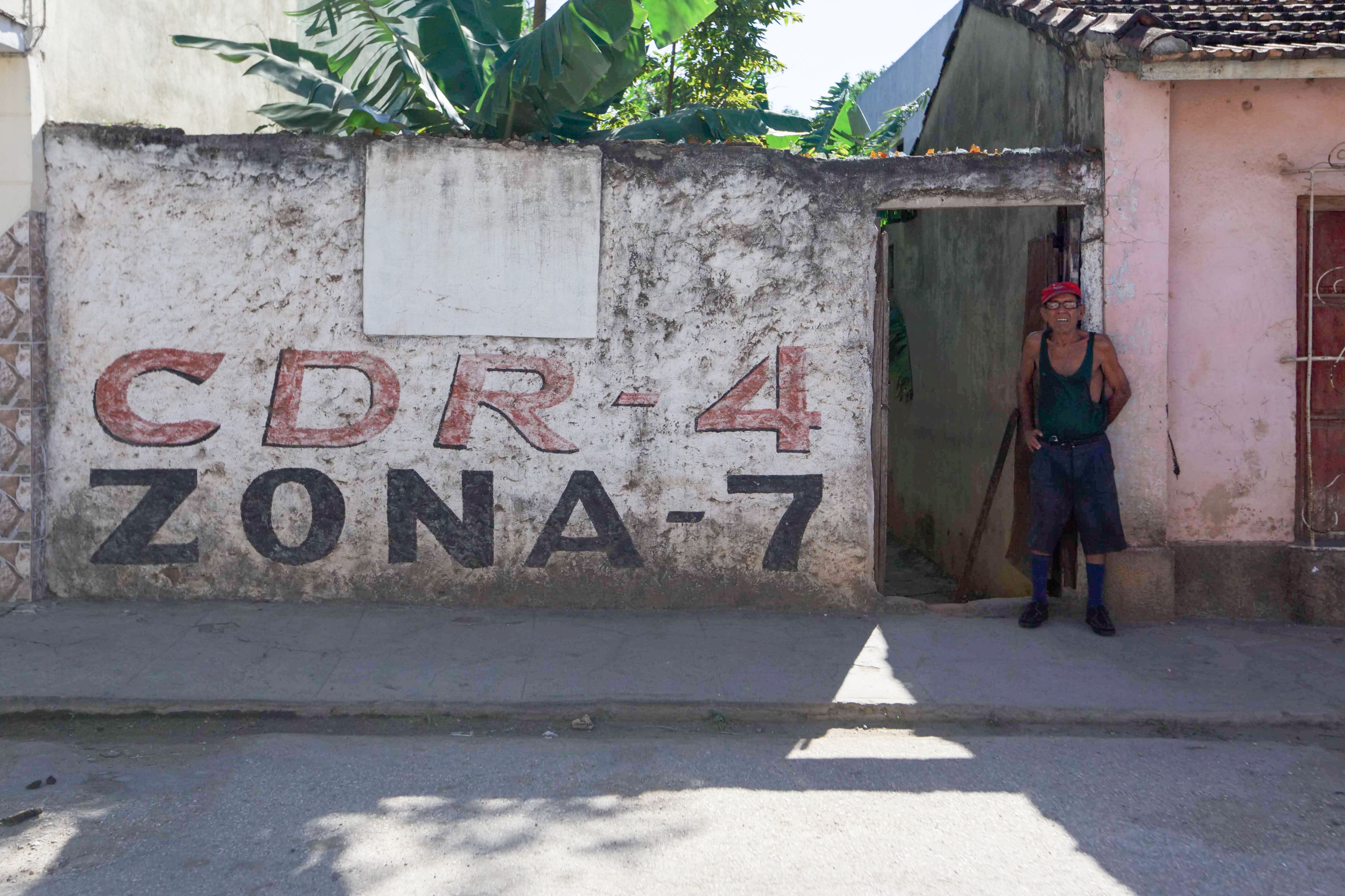 A man stands in a doorway beside a weathered concrete wall in an urban neighborhood.