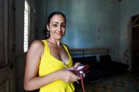 A smiling woman in a yellow top holding a purse. Captured indoors with natural lighting.