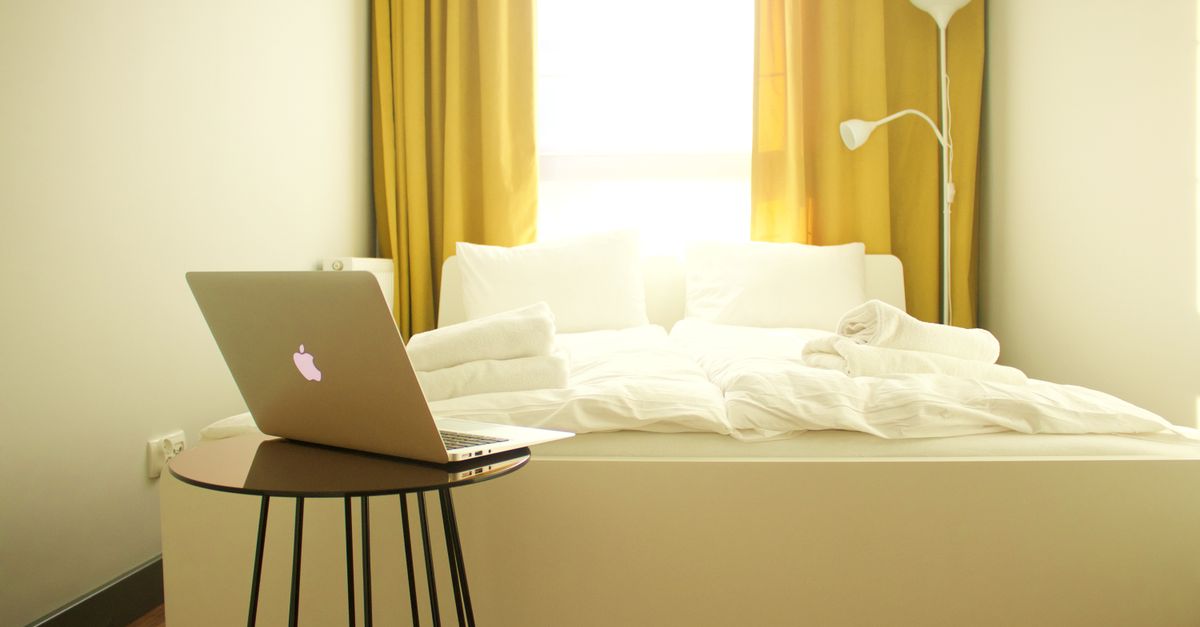 Quarto aconchegante com um laptop, cortinas amarelas e decoração contemporânea.