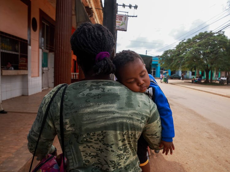 Woman Carrying Sleeping Baby On City Street